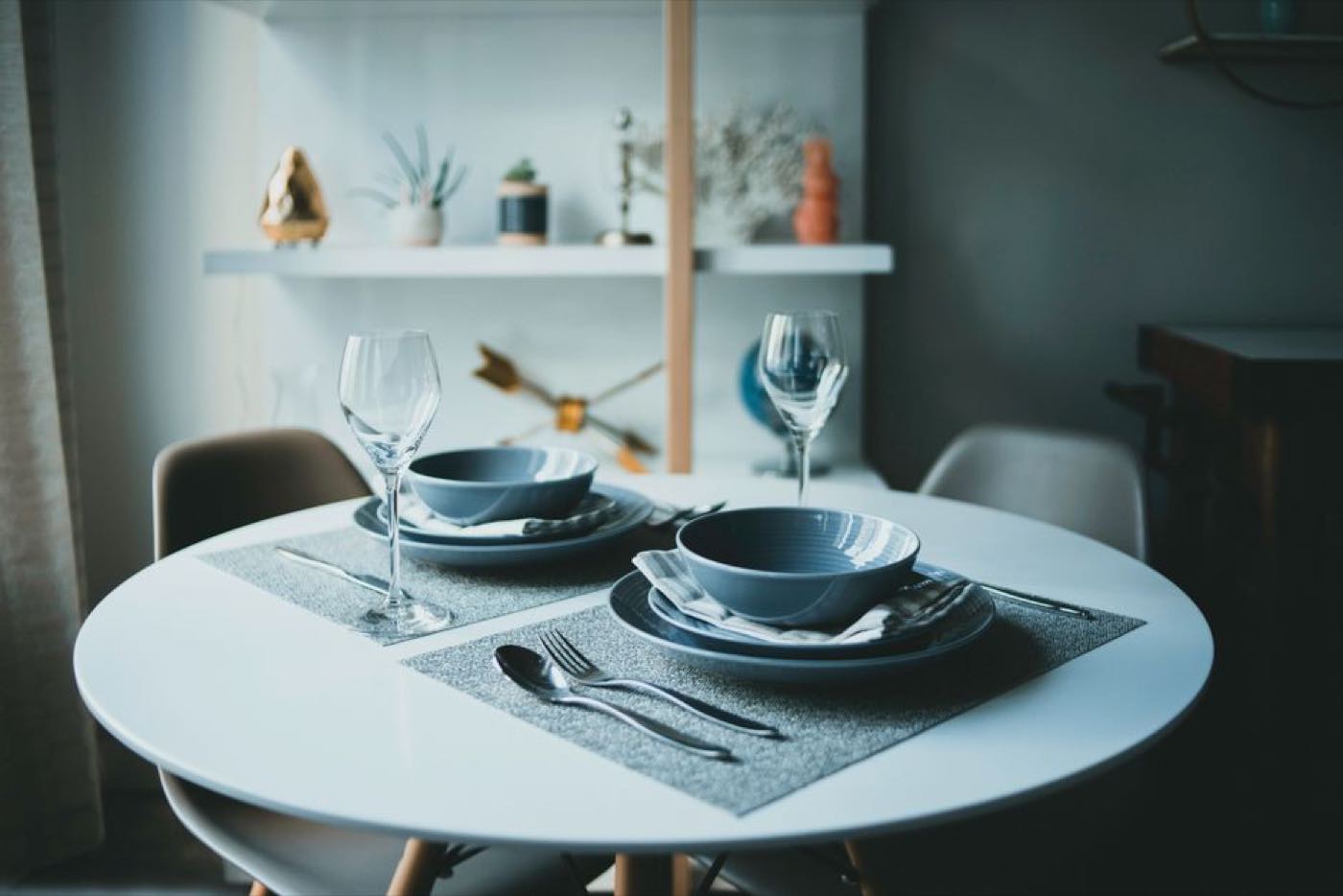 A round table laid for two, with bowls, glasses and cutlery on grey placemats.