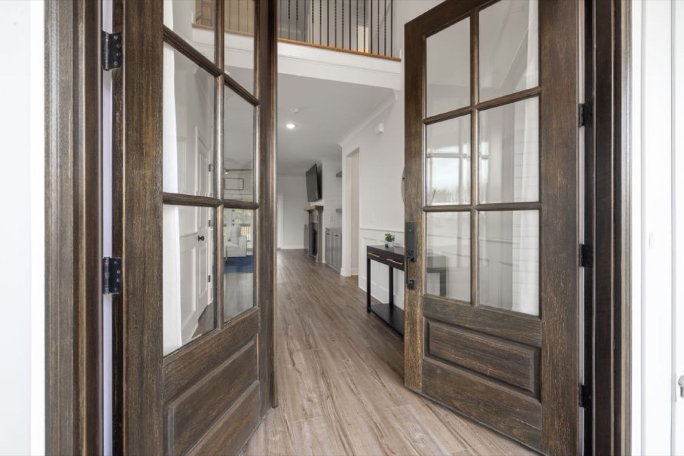 An entrance hall with wooden glazed double doors open onto a bright hallway and console table.
