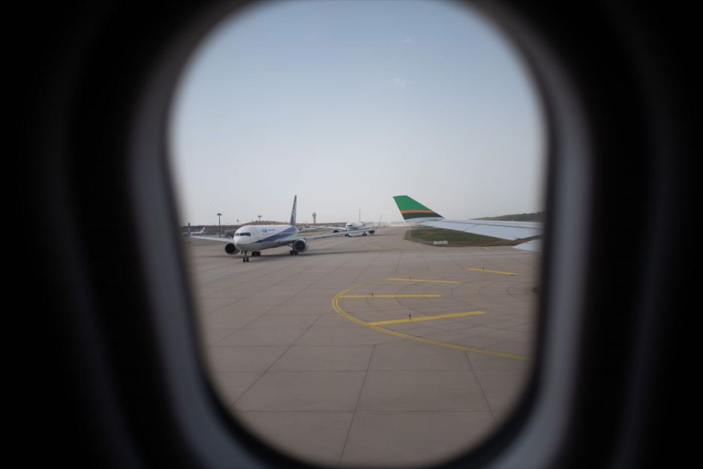 The view from an aircraft window across the apron, with parked aircraft and taxiway markings.