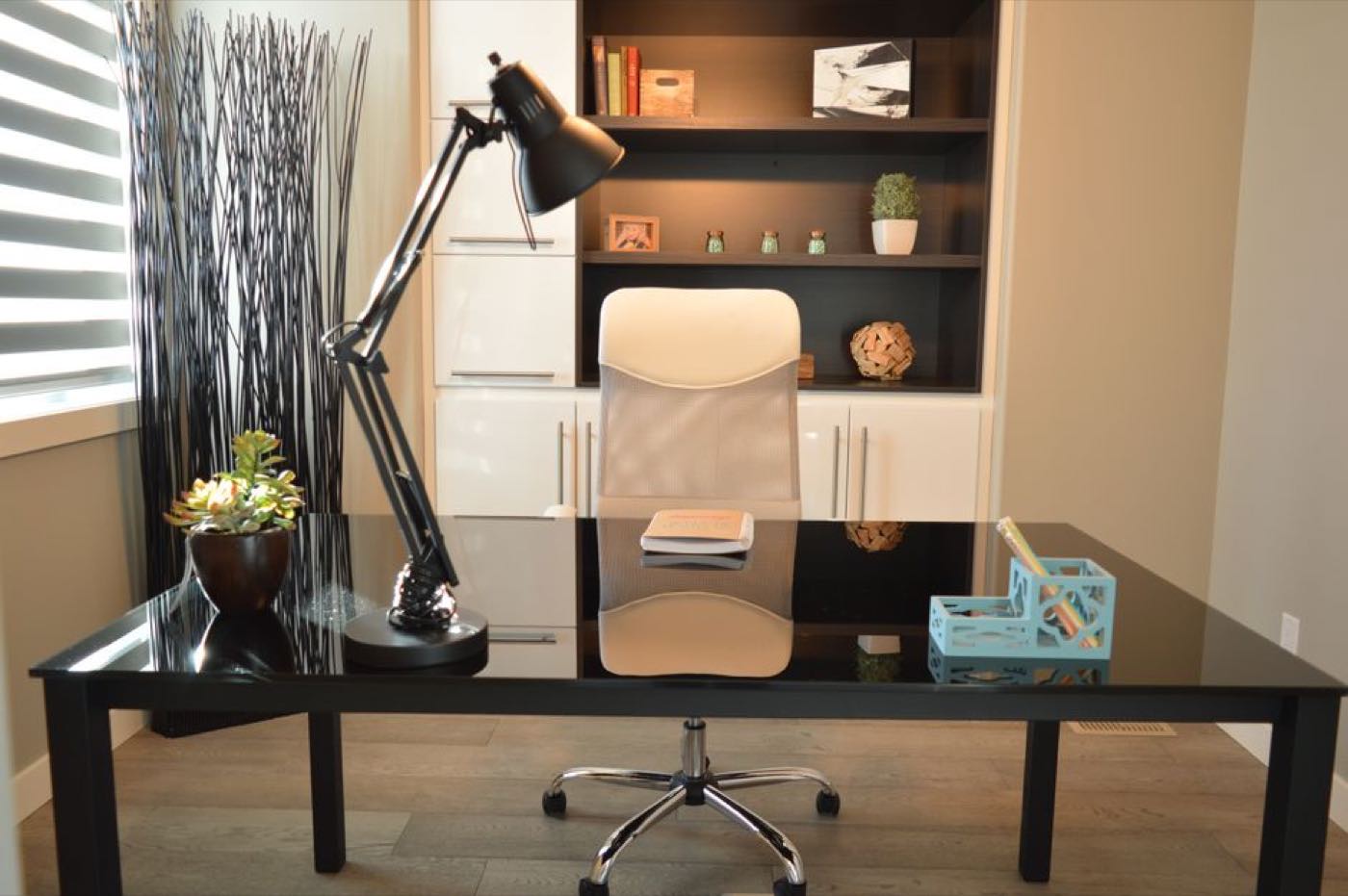 A home office with a white mesh desk chair pulled up to a dark desk beside a window.