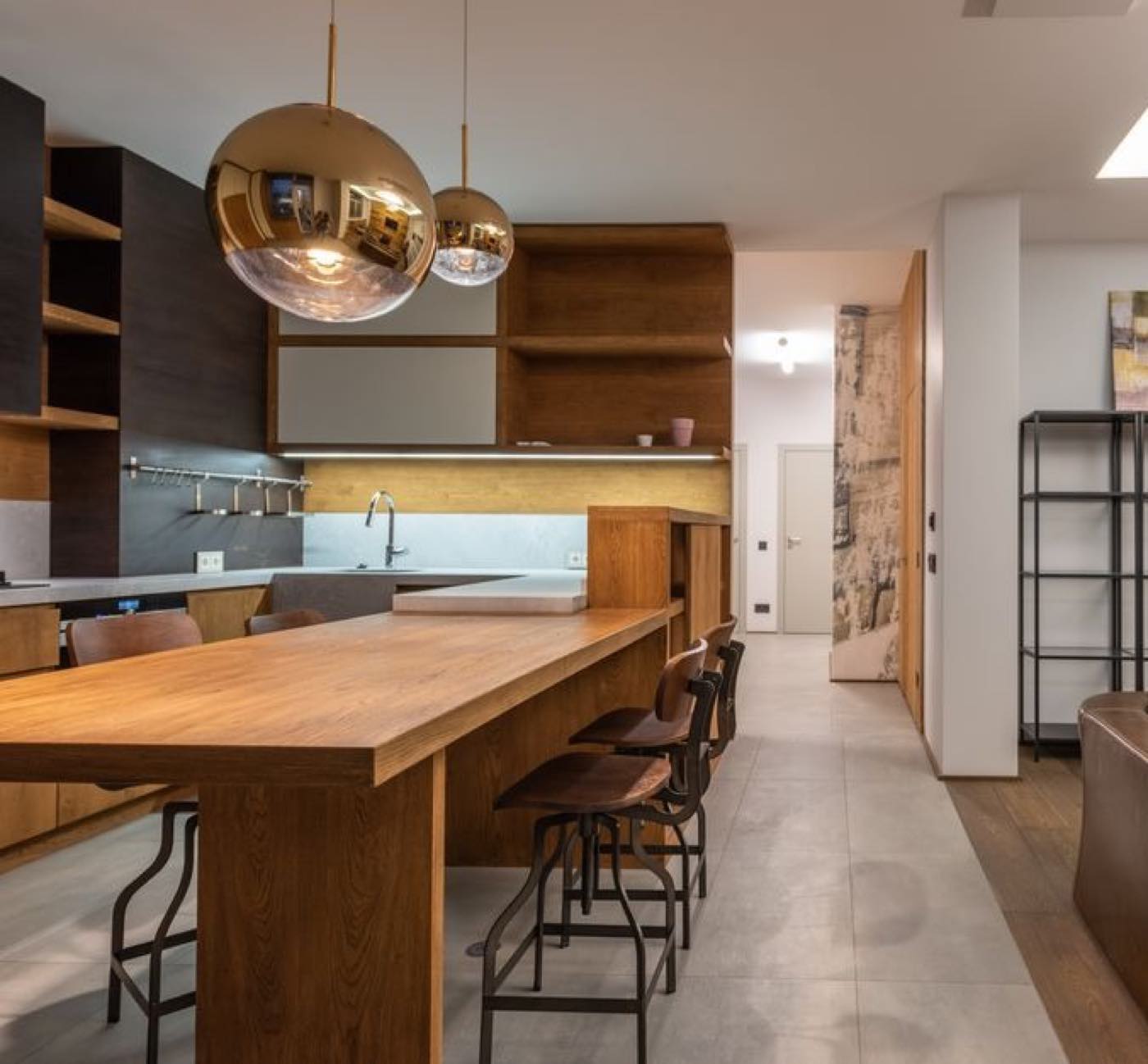 An open-plan kitchen with a long wooden breakfast bar, stools and brass pendant lights.